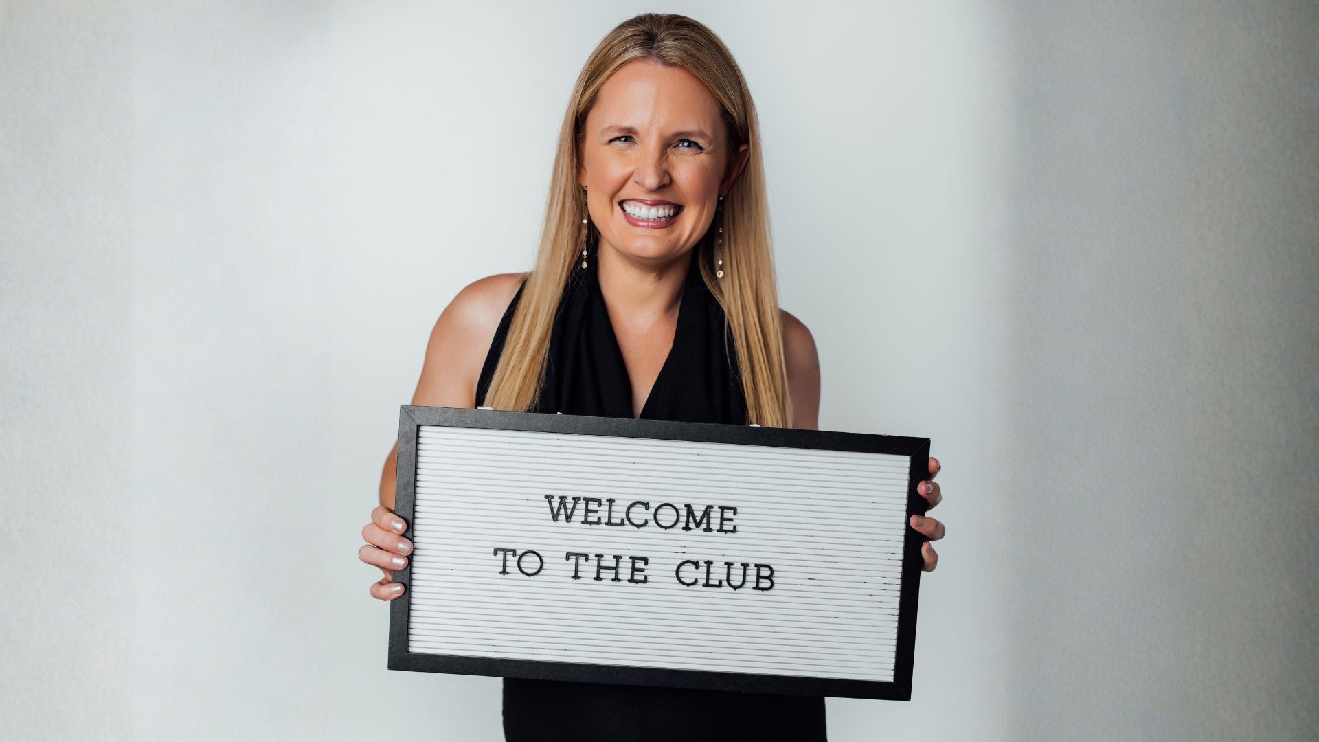 Woman holding a sign that says 'Welcome to the Club' 